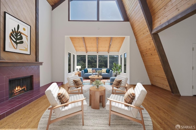 living area featuring wood finished floors, high vaulted ceiling, wood ceiling, and a tile fireplace