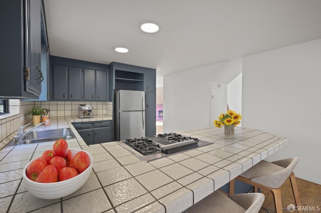 kitchen featuring a sink, open shelves, a peninsula, appliances with stainless steel finishes, and tile counters