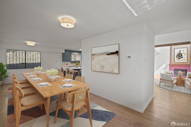 dining space with baseboards, a brick fireplace, and light wood finished floors