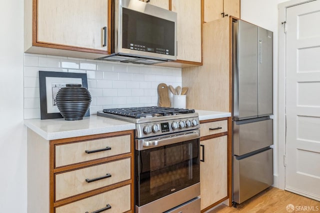 kitchen featuring light brown cabinetry, light wood-type flooring, backsplash, and appliances with stainless steel finishes