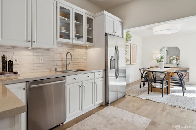 kitchen featuring backsplash, light wood-style flooring, appliances with stainless steel finishes, white cabinets, and a sink