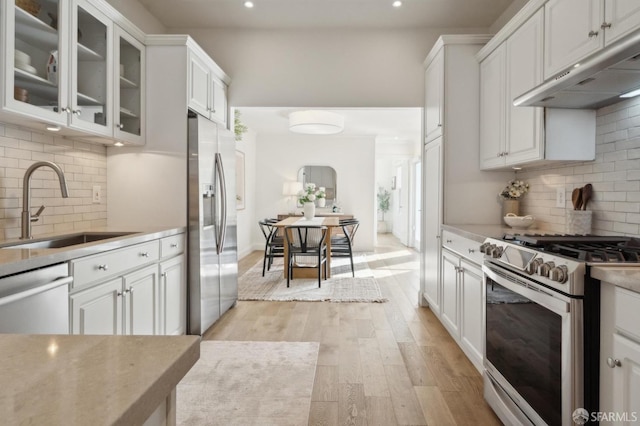 kitchen featuring appliances with stainless steel finishes, white cabinets, a sink, light wood-type flooring, and under cabinet range hood