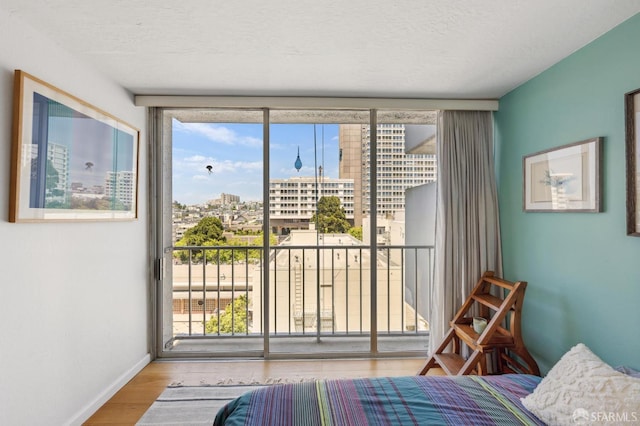 bedroom featuring access to outside, wood finished floors, a view of city, and baseboards