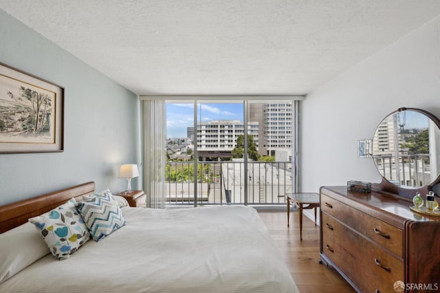 bedroom with a wall of windows, wood finished floors, a textured ceiling, and a city view