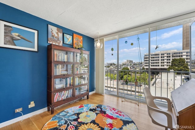 sitting room featuring a wall of windows, a textured ceiling, wood finished floors, baseboards, and a view of city