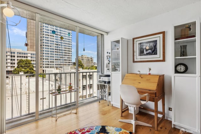 dining space featuring a city view, wood-type flooring, expansive windows, a textured ceiling, and baseboards