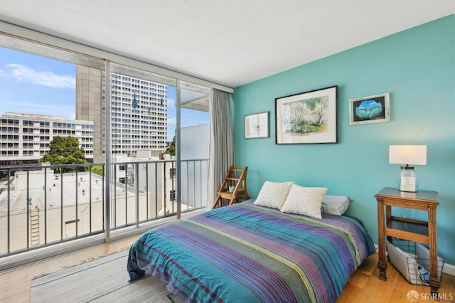 bedroom with wood finished floors, access to exterior, and floor to ceiling windows