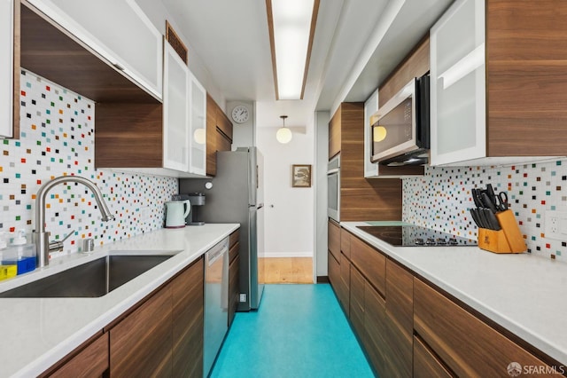 kitchen featuring stainless steel appliances, a sink, light countertops, decorative backsplash, and glass insert cabinets