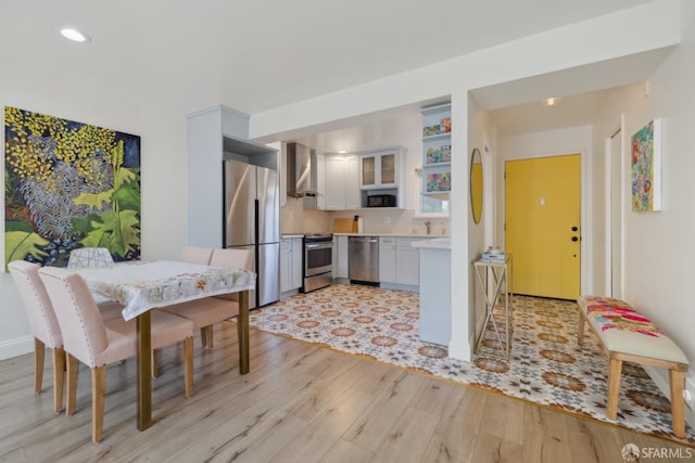 kitchen with sink, light wood-type flooring, appliances with stainless steel finishes, white cabinets, and wall chimney range hood