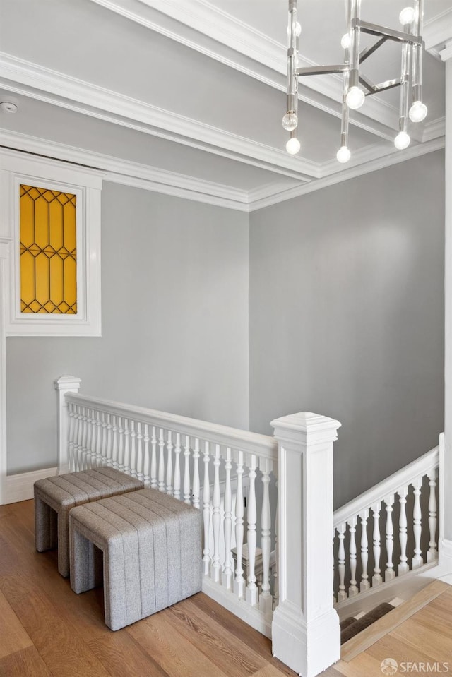 corridor featuring ornamental molding, wood finished floors, an upstairs landing, and an inviting chandelier