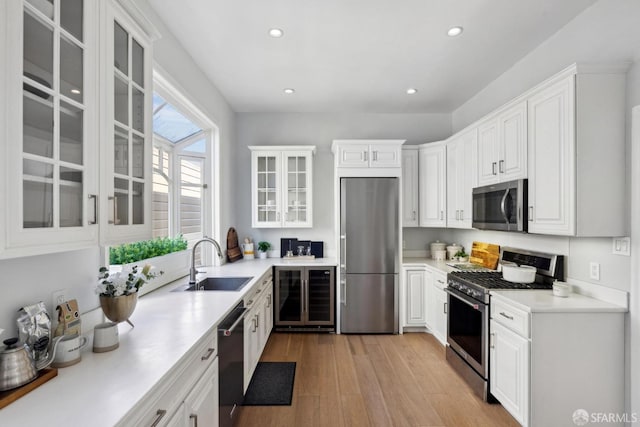 kitchen with light wood finished floors, wine cooler, appliances with stainless steel finishes, white cabinetry, and a sink