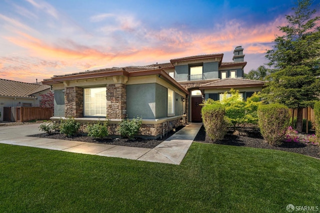 prairie-style house featuring a tile roof, stone siding, fence, a front yard, and stucco siding