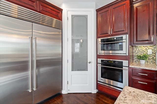 kitchen featuring dark wood finished floors, light stone counters, stainless steel appliances, reddish brown cabinets, and tasteful backsplash