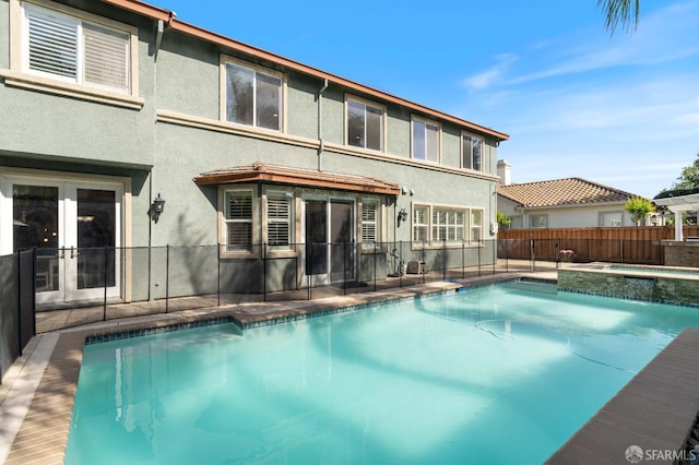 view of pool with fence, a pool with connected hot tub, and french doors