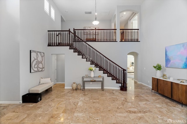 staircase with marble finish floor, arched walkways, baseboards, a high ceiling, and visible vents