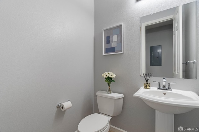 half bathroom featuring toilet, a sink, electric panel, and baseboards