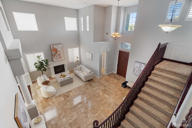 living area with stairs, a fireplace with raised hearth, baseboards, a high ceiling, and a notable chandelier