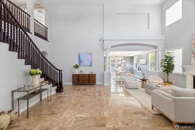 living room featuring marble finish floor, a towering ceiling, visible vents, decorative columns, and stairs