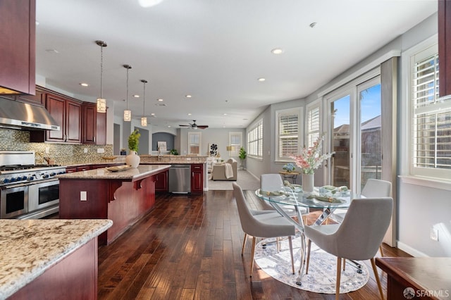 kitchen featuring stainless steel appliances, a peninsula, dark wood-style flooring, open floor plan, and under cabinet range hood