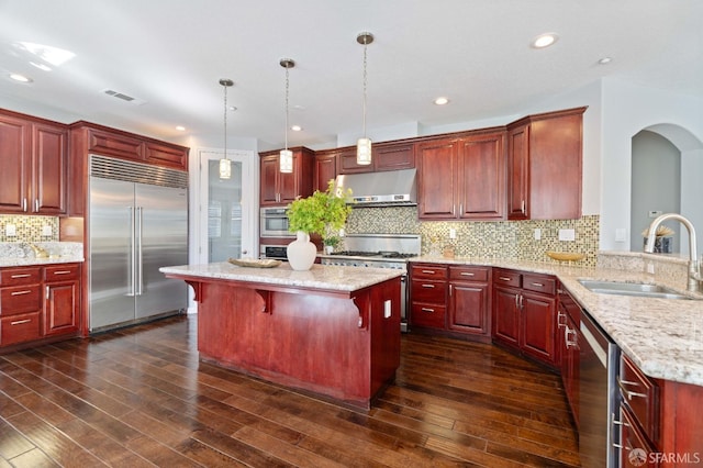 kitchen featuring under cabinet range hood, premium appliances, visible vents, reddish brown cabinets, and a sink