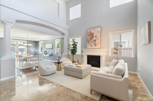 living room featuring baseboards, a glass covered fireplace, a towering ceiling, and ornate columns