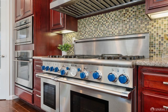 kitchen with reddish brown cabinets, dark wood-type flooring, light stone countertops, decorative backsplash, and custom exhaust hood