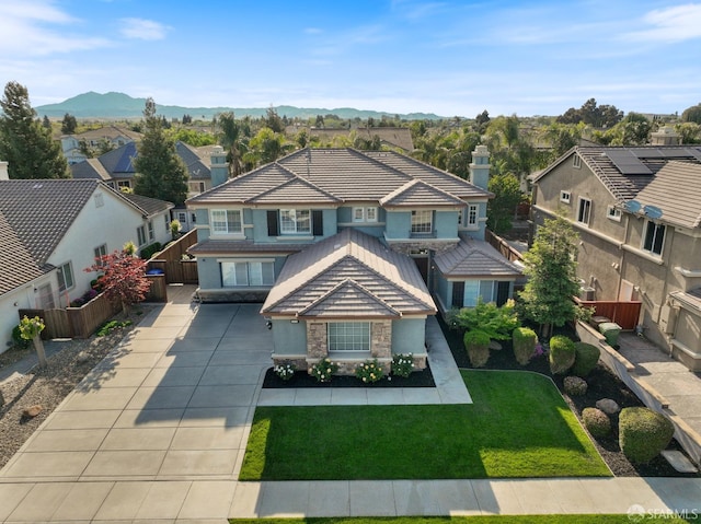 view of front of property featuring driveway, stone siding, a tiled roof, fence, and a residential view