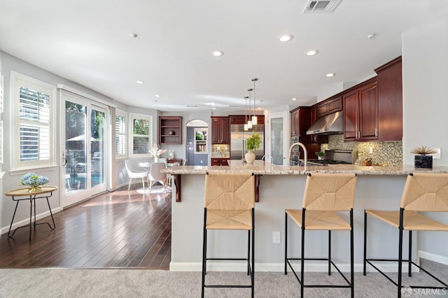kitchen with a peninsula, visible vents, recessed lighting, light stone countertops, and under cabinet range hood