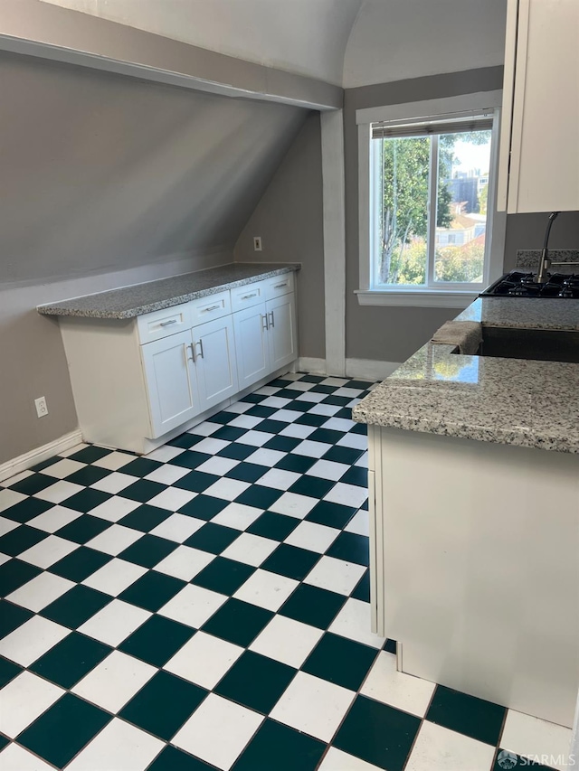 kitchen featuring vaulted ceiling, white cabinets, light floors, and baseboards