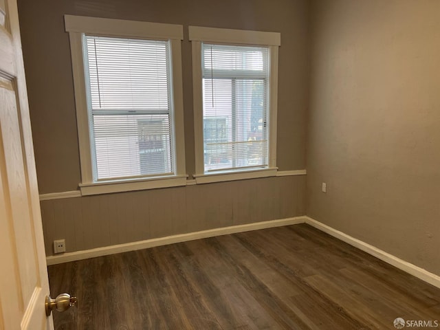 unfurnished room featuring dark wood-style floors, wainscoting, and baseboards