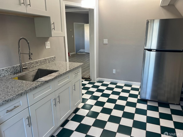 kitchen with tile patterned floors, a sink, white cabinetry, freestanding refrigerator, and baseboards