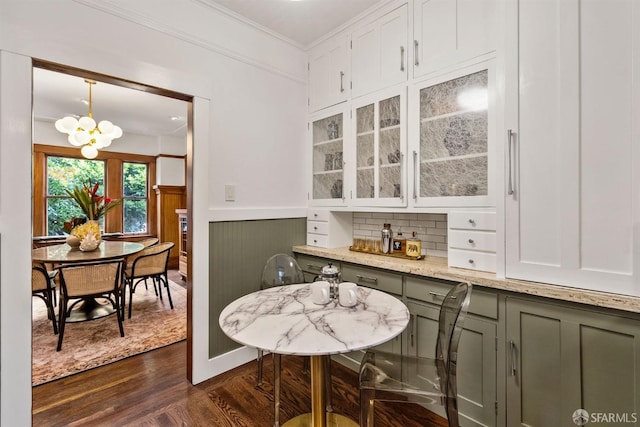 bar featuring dark wood-type flooring, crown molding, an inviting chandelier, decorative light fixtures, and white cabinets