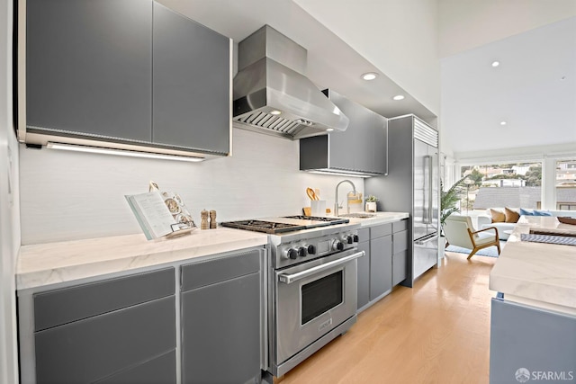 kitchen featuring gray cabinetry, a sink, light wood-style floors, wall chimney exhaust hood, and high end appliances