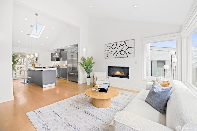 living area featuring a skylight, light wood finished floors, recessed lighting, a glass covered fireplace, and baseboards