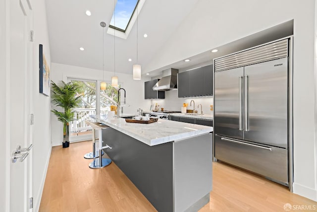 kitchen featuring light wood finished floors, wall chimney range hood, a skylight, and built in fridge