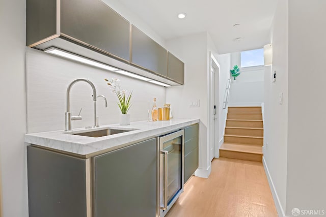 bar featuring beverage cooler, a sink, baseboards, stairway, and light wood finished floors