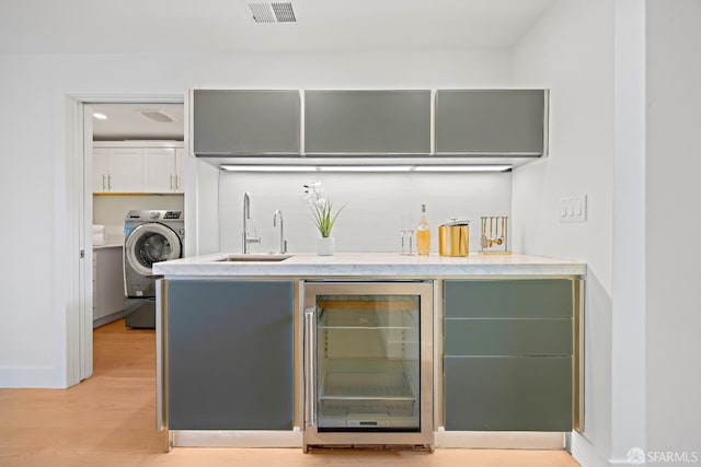 bar featuring visible vents, a sink, washer / dryer, beverage cooler, and bar