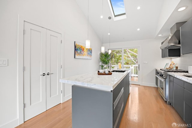 kitchen with high end stove, gray cabinetry, a sink, light wood-style floors, and wall chimney range hood