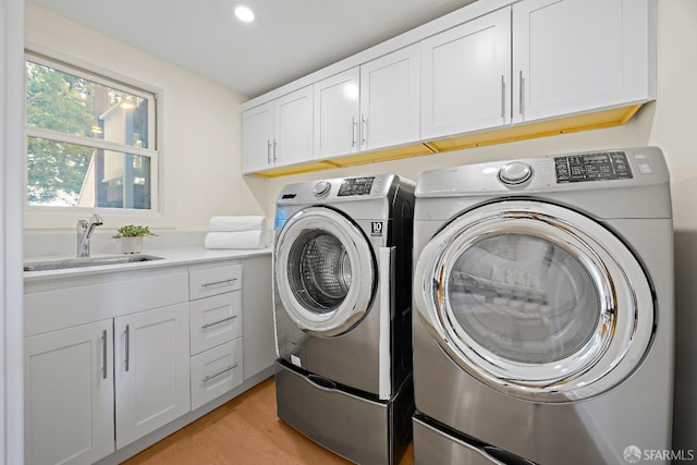 laundry area with light wood-type flooring, cabinet space, washing machine and dryer, and a sink