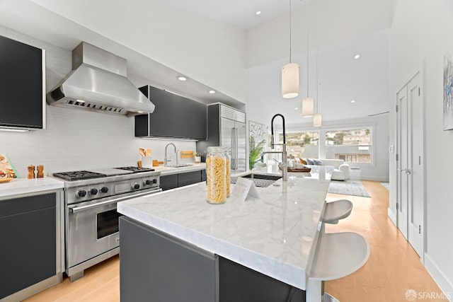 kitchen with light wood-style flooring, a kitchen breakfast bar, high end stainless steel range oven, dark cabinetry, and wall chimney range hood