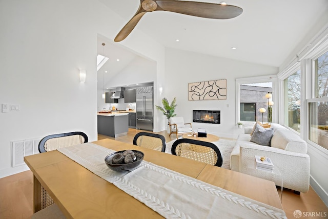 dining area with visible vents, a glass covered fireplace, light wood-type flooring, high vaulted ceiling, and recessed lighting