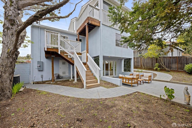 rear view of property featuring a patio, outdoor lounge area, central AC unit, fence, and stairs