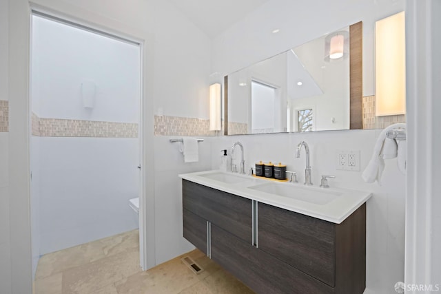 bathroom featuring double vanity, a sink, and tile walls