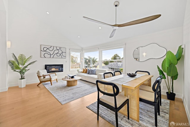 dining space with light wood-type flooring, high vaulted ceiling, baseboards, and a glass covered fireplace