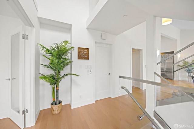 corridor with light wood-style floors, lofted ceiling, stairway, and baseboards