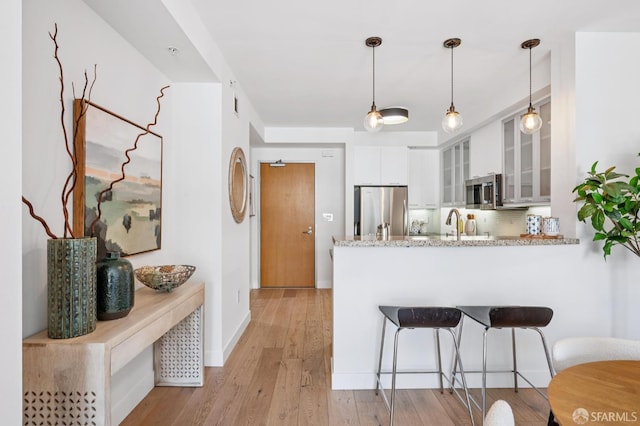 170 King St Unit 1006, San Francisco, CA 94107 - kitchen featuring stainless steel appliances, a peninsula, white cabinetry, glass insert cabinets, and a kitchen bar