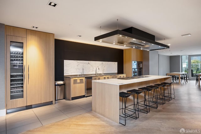 kitchen with decorative backsplash, light hardwood / wood-style floors, a kitchen island, stainless steel appliances, and island exhaust hood