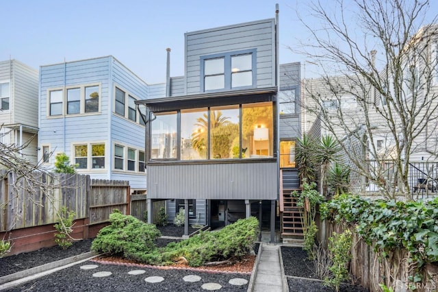 rear view of house featuring stairway, fence, and a sunroom