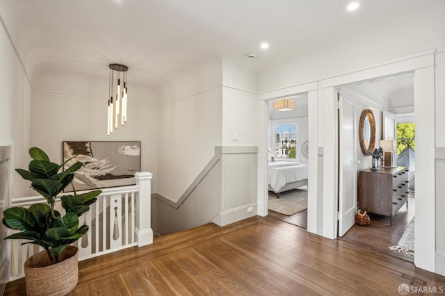 hall with recessed lighting, a decorative wall, wood finished floors, and an upstairs landing