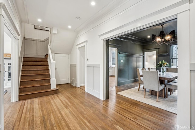 dining area with a decorative wall, wood finished floors, ornamental molding, stairway, and an inviting chandelier